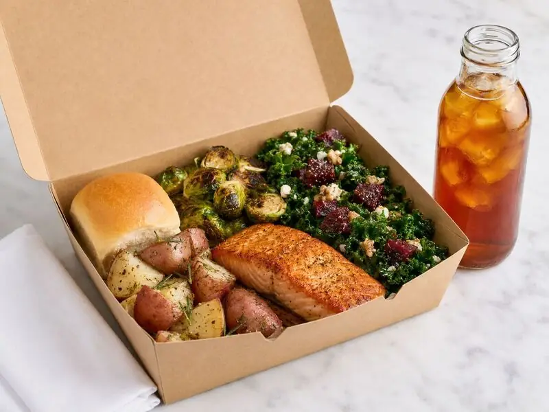 Concord individually packaged dinner from Winslow’s Catering featuring seasoned salmon, roasted vegetables, red potatoes, a roll, and tea.