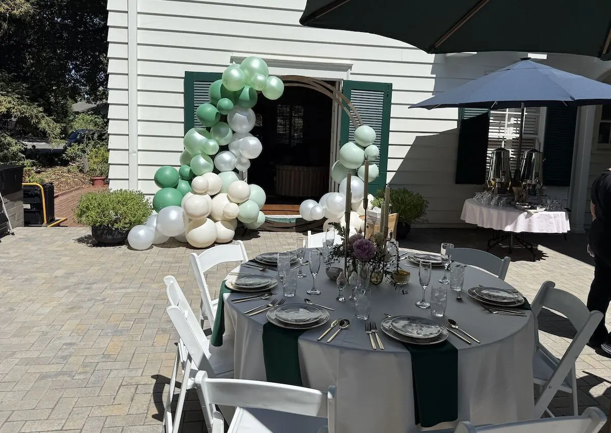 Sage and ivory balloon arch over an archway paired with a styled table — balloon and floral styling for Brentwood catering and Concord milestone parties