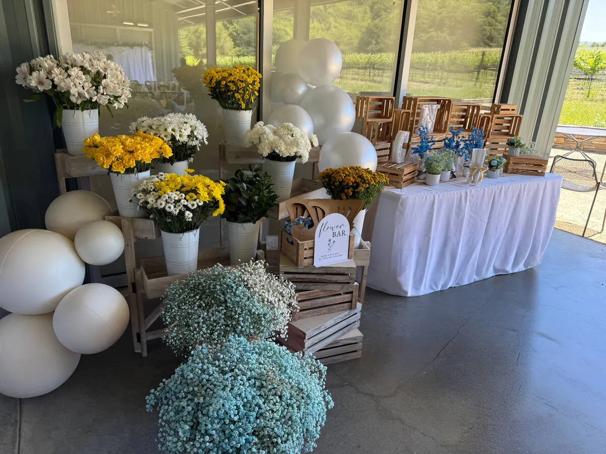 Bloom bar of buckets holding yellow roses, daisies and baby's breath set out for guests to wrap take-home bouquets — signature bloom bar from our Concord catering team