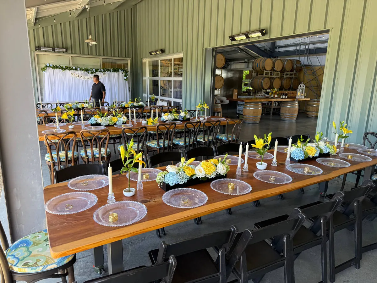 Long table lined with yellow lily, blue hydrangea and white rose centerpieces between taper candles — centerpiece design for Hercules catering and Concord receptions